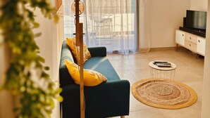 Una sala de estar moderna con un sofá, un televisor, una mesita redonda y una lámpara colgante.
