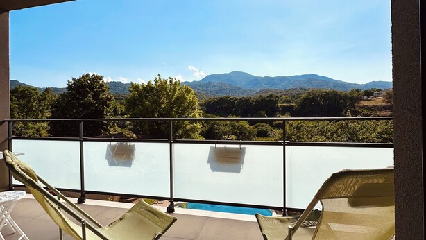 Un balcón con dos sillones de descanso, una piscina y vistas a las montañas.