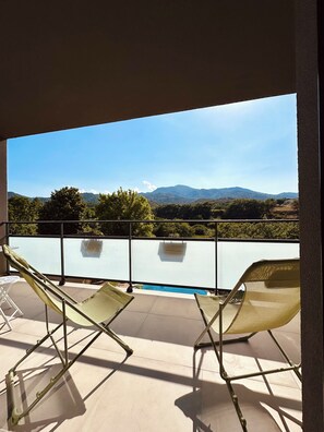En balkong med två solstolar, en pool och utsikt över bergen.