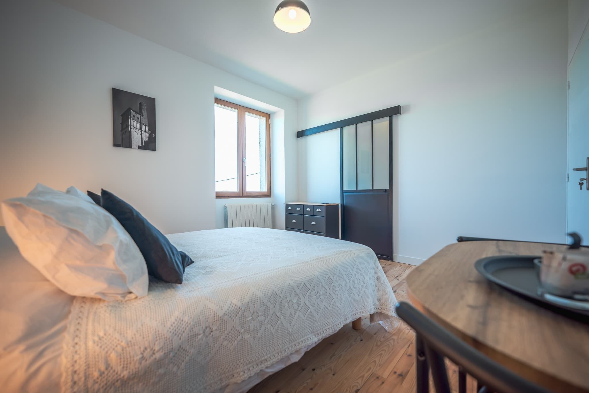 A bedroom with a bed, a window, a radiator, a wardrobe, and a table with a tray.
