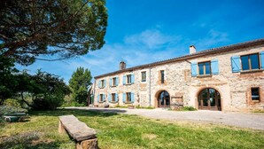A stone building with a central entrance, arched doorways, and blue shutters. - Les Jardins de la Longagne (Saussenac)