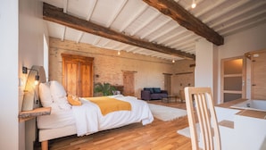 A bedroom with a bed, bedside table, lamp, wooden beams, brick wall, and a window. - Les Jardins de la Longagne (Saussenac)