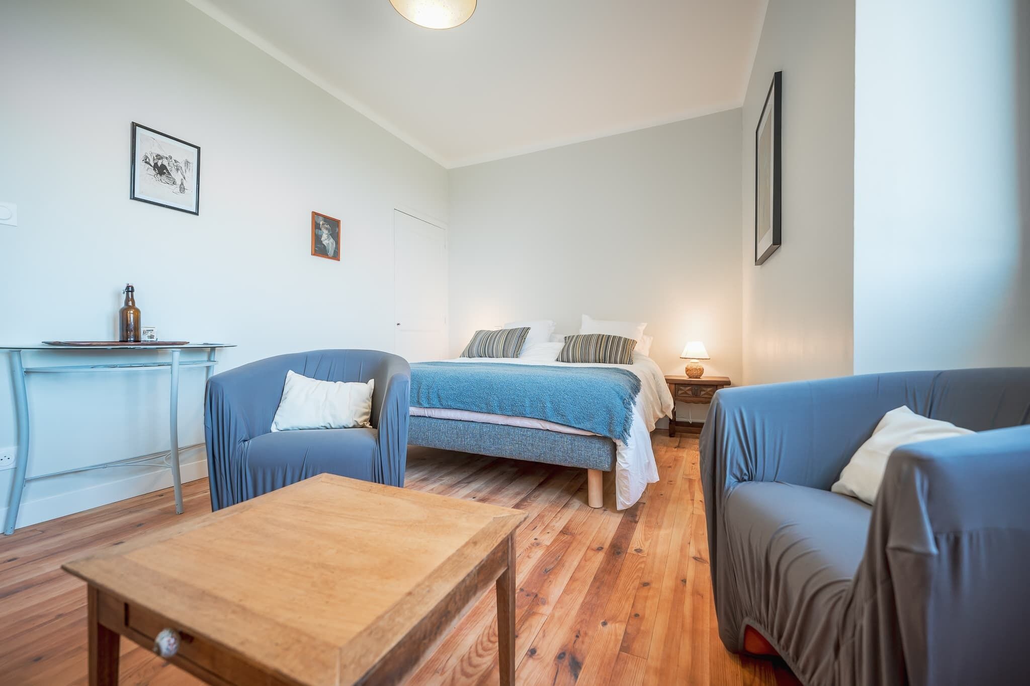 Una habitación con una cama, dos sofás, una mesa de madera y una mesita con una botella.