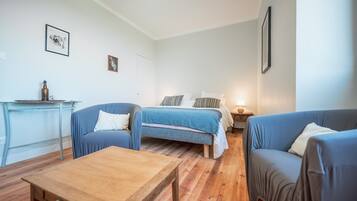 Una habitación con una cama, dos sofás, una mesa de madera y una mesita con una botella.