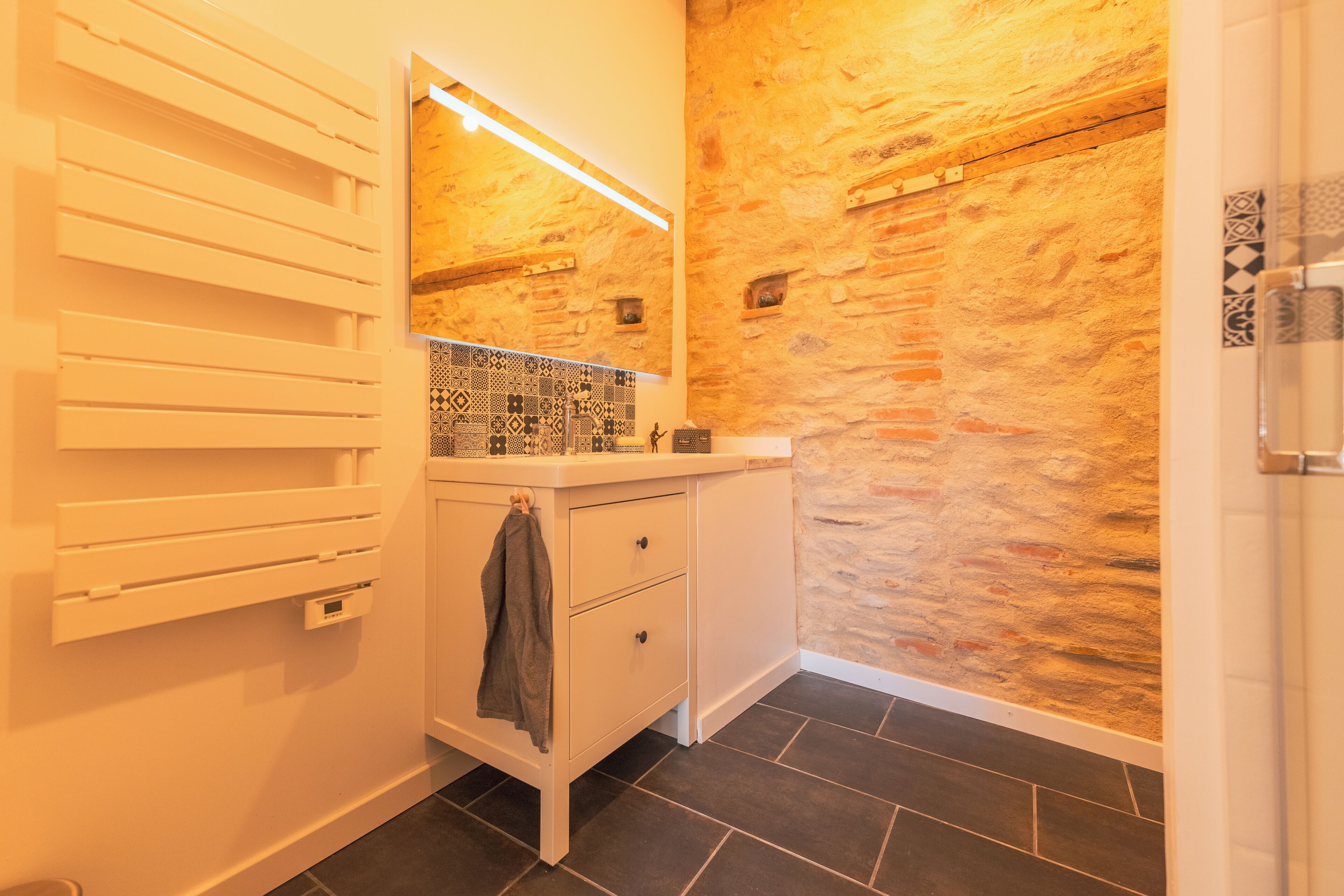A bathroom with a stone wall, a white vanity, a mirror, and a towel rack.