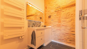 A bathroom with a stone wall, a white vanity, a mirror, and a towel rack.
