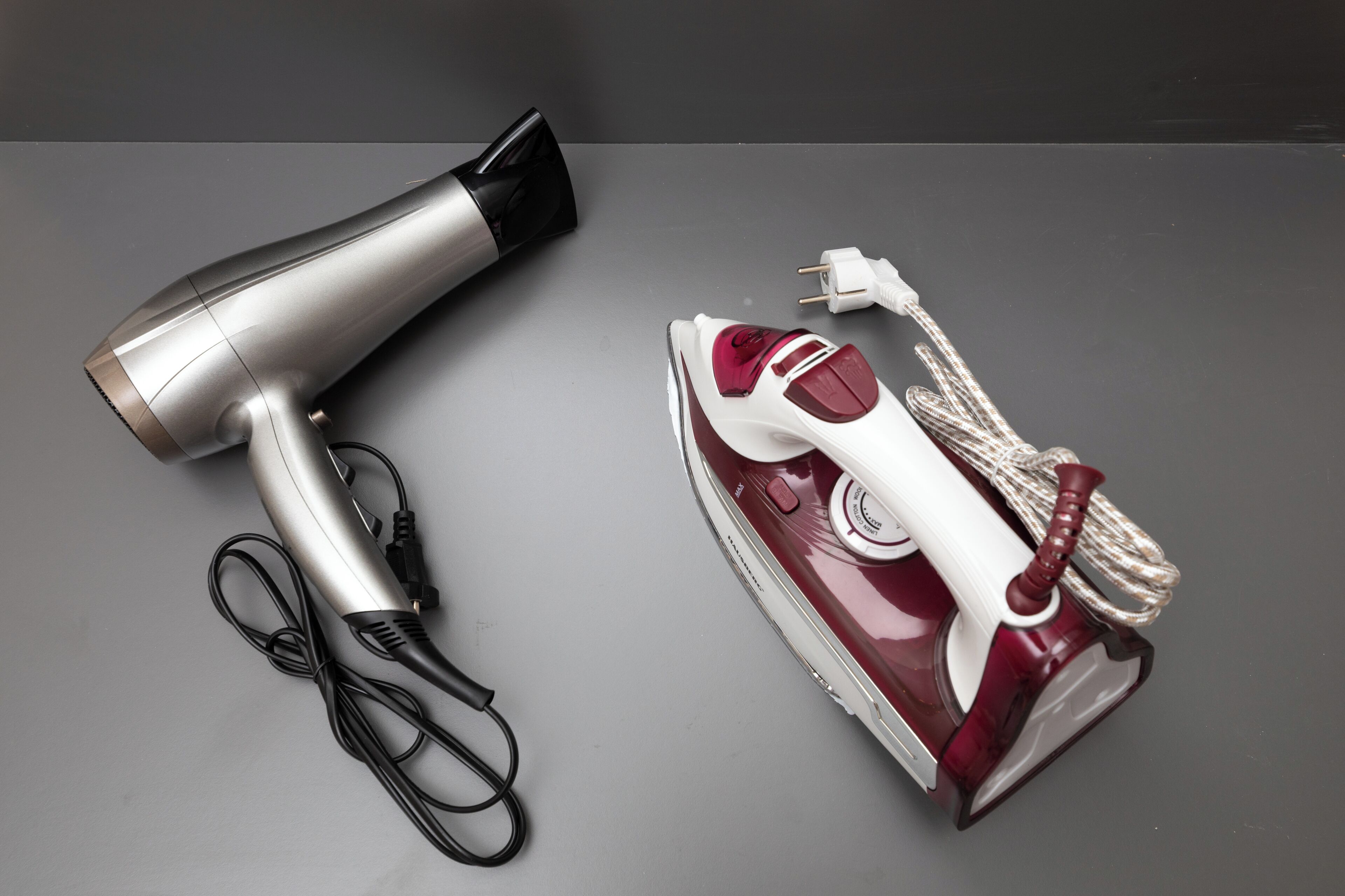 A hair dryer and an iron on a grey surface.
