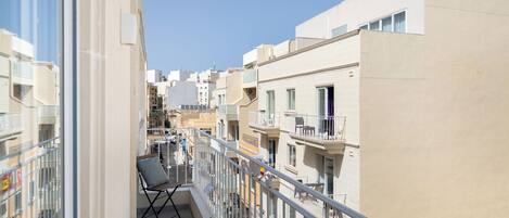A balcony with a chair, railing, and a view of neighboring buildings.