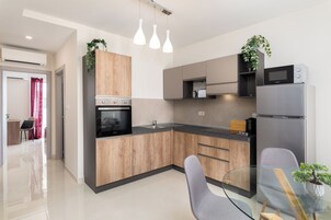 Una cocina moderna con armarios de madera, un refrigerador de acero inoxidable, un horno empotrado y una mesa de comedor de vidrio.