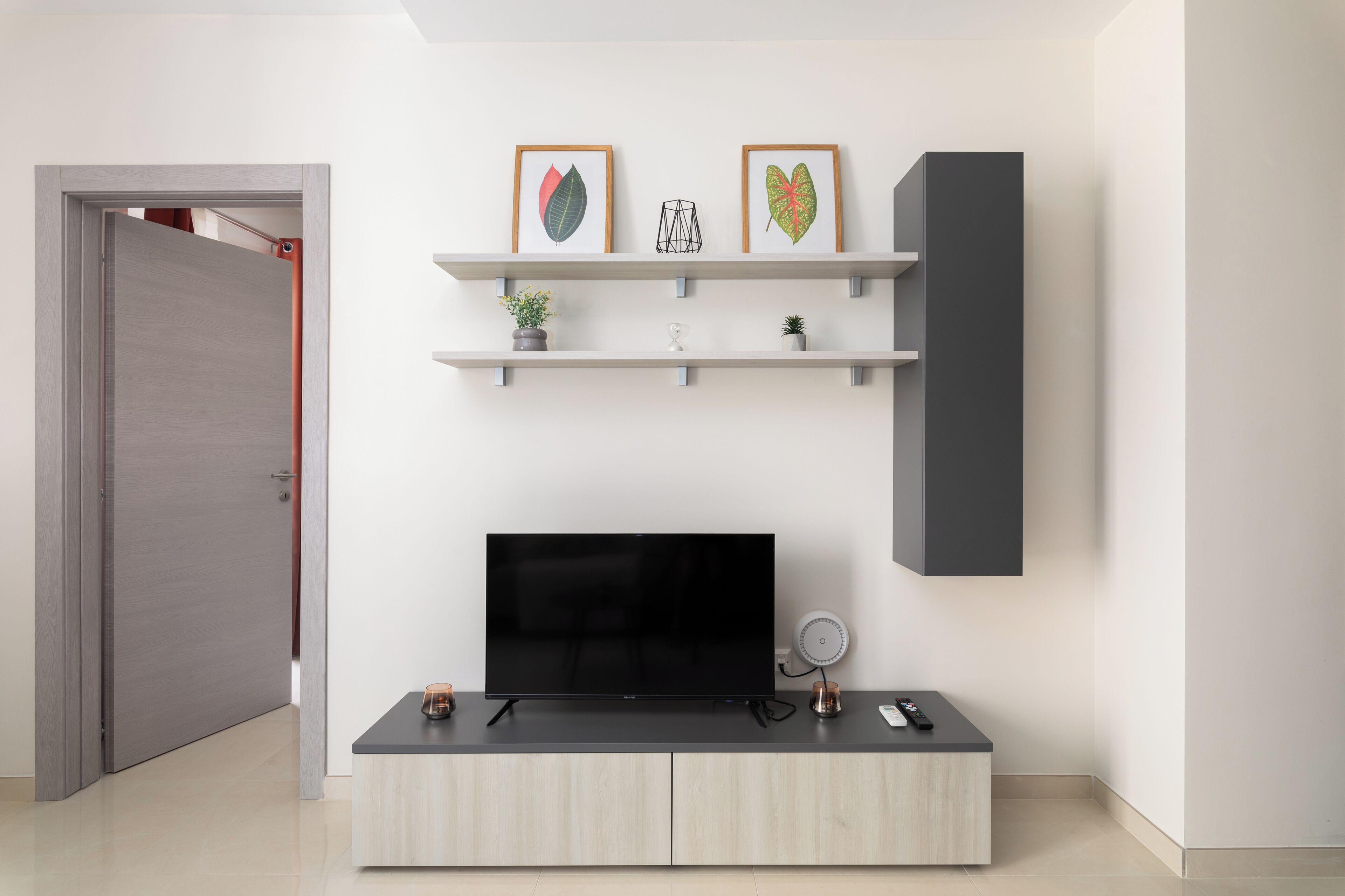 Een moderne woonkamer met een flatscreen televisie, een bijzettafeltje en een minimalistische boekenkast met decoratieve objecten.