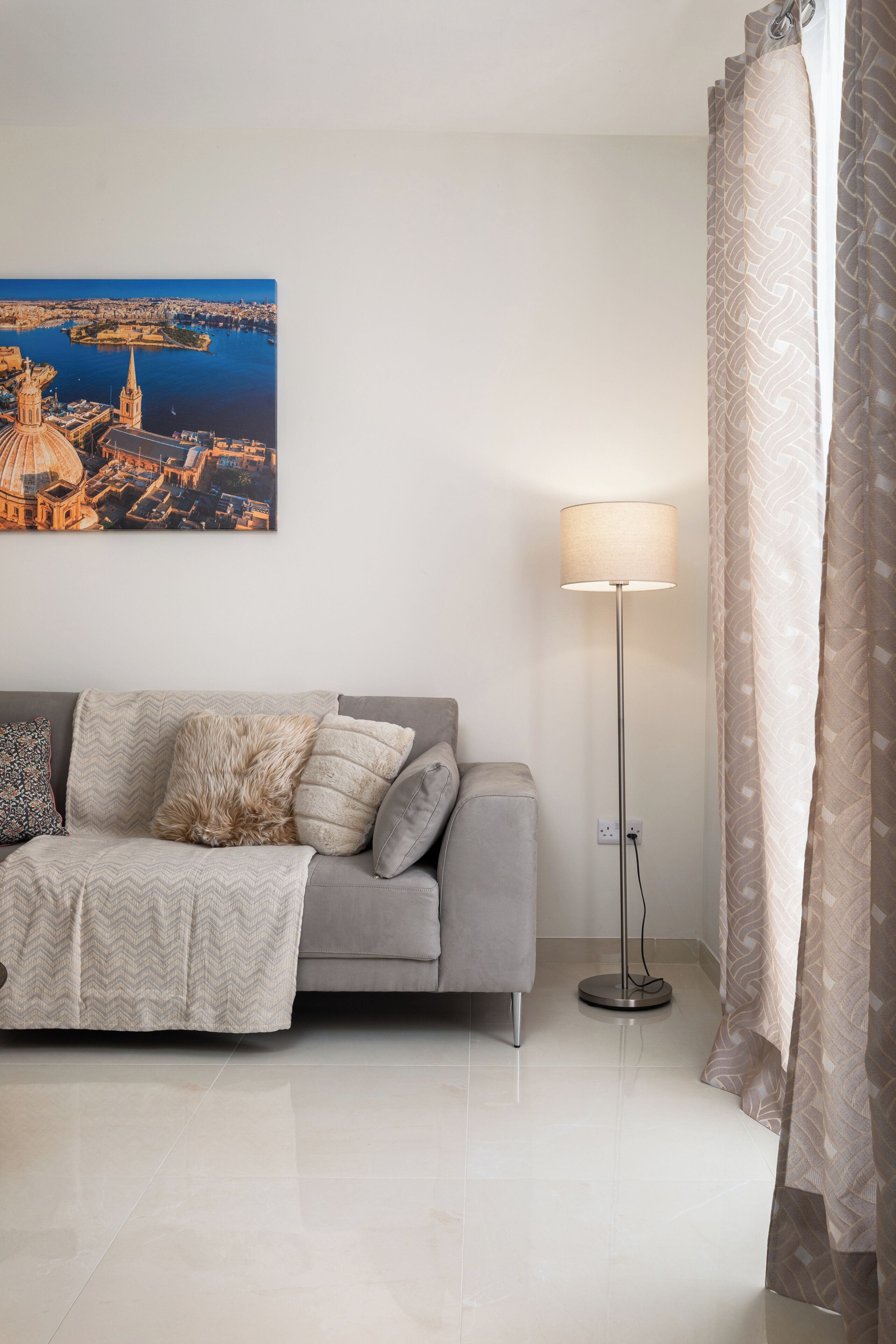 A modern living room with a sofa, a floor lamp, and a cityscape painting.