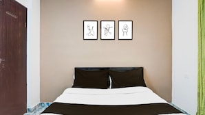 Ein Hotelzimmer mit einem Bett, einem Kopfteil, einer Wandleuchte und drei gerahmten Kunstwerken.