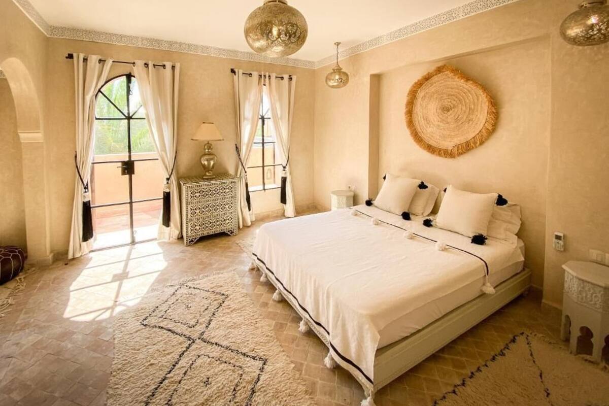 Un dormitorio amplio con una cama grande, un tapiz redondo tejido en la pared y vistas a través de una ventana con cortinas.