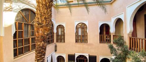 A courtyard with a palm tree, arched windows, and a table with chairs.