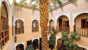 A courtyard with a palm tree, arched windows, and potted plants. - Riad Selouane (Marrakech)