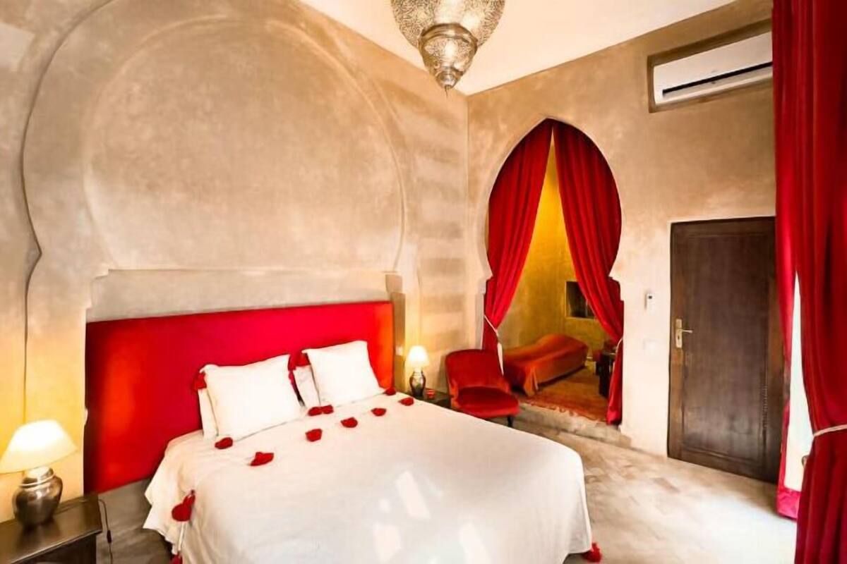 Habitación de hotel con una cama grande, dosel rojo, una silla roja y una puerta con cortinas rojas.