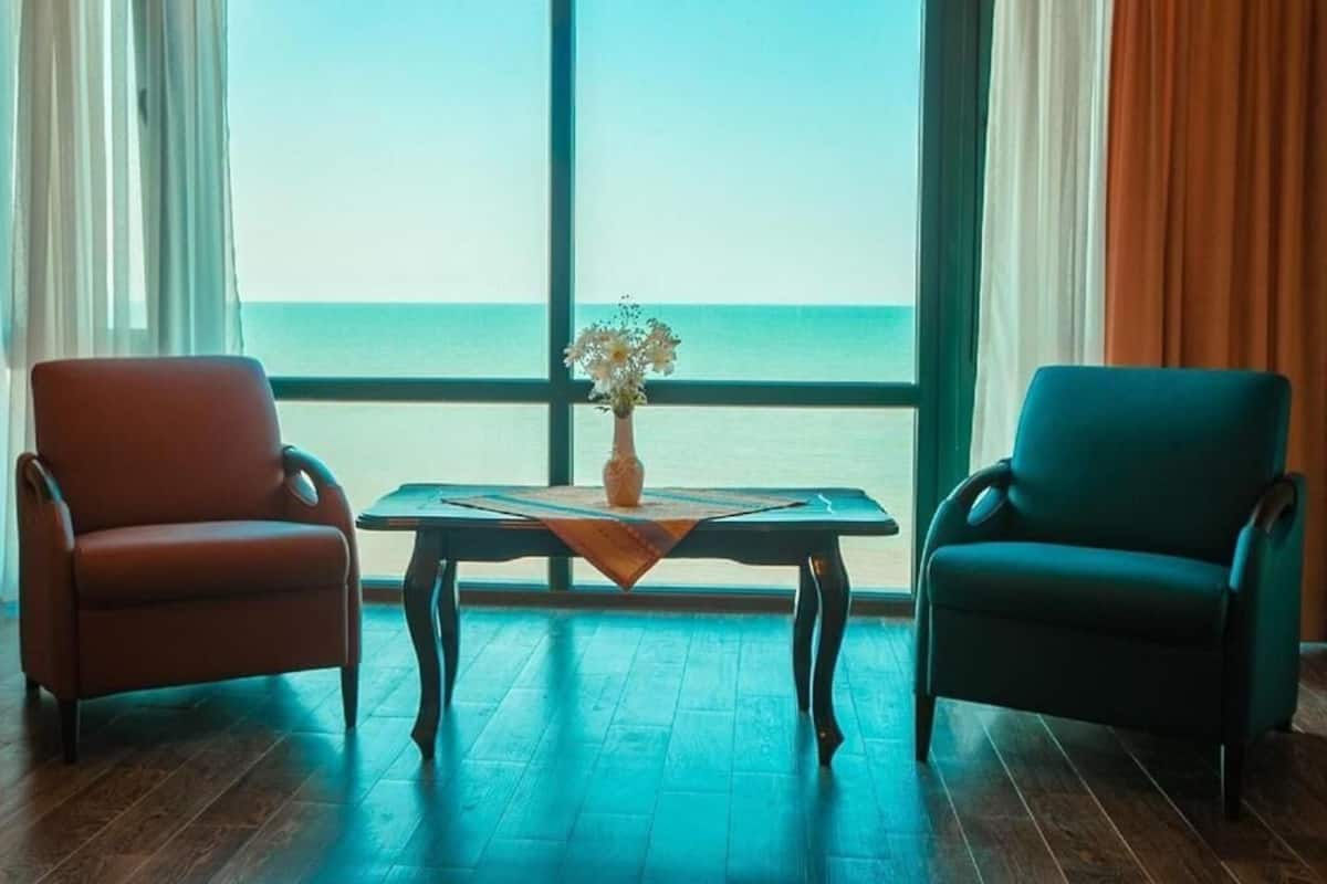 A room with two chairs, a table, and a view of the sea through large windows.