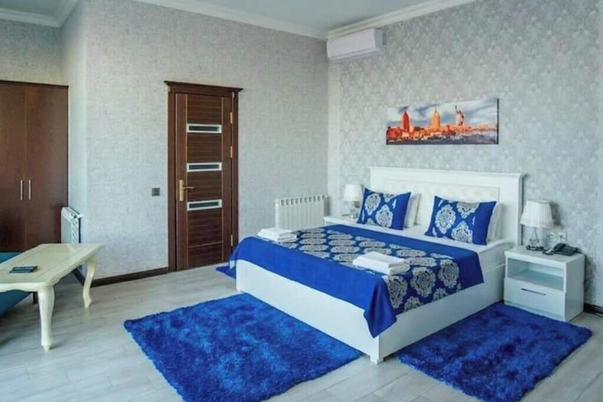 A bedroom with a bed, bedside tables, a desk, a chair, a radiator, and a door.