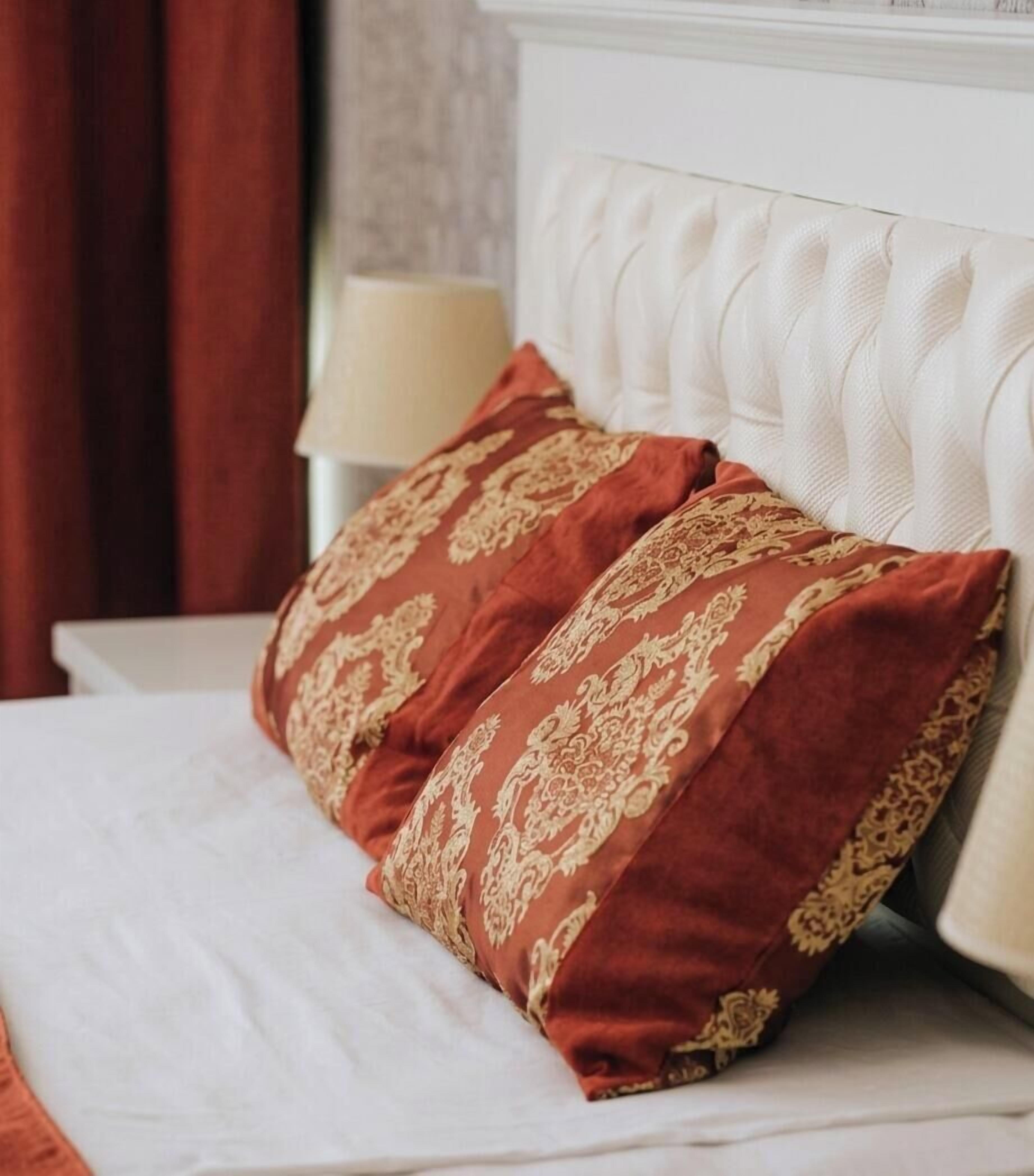 A bed with a white headboard and two red pillows with gold patterns.