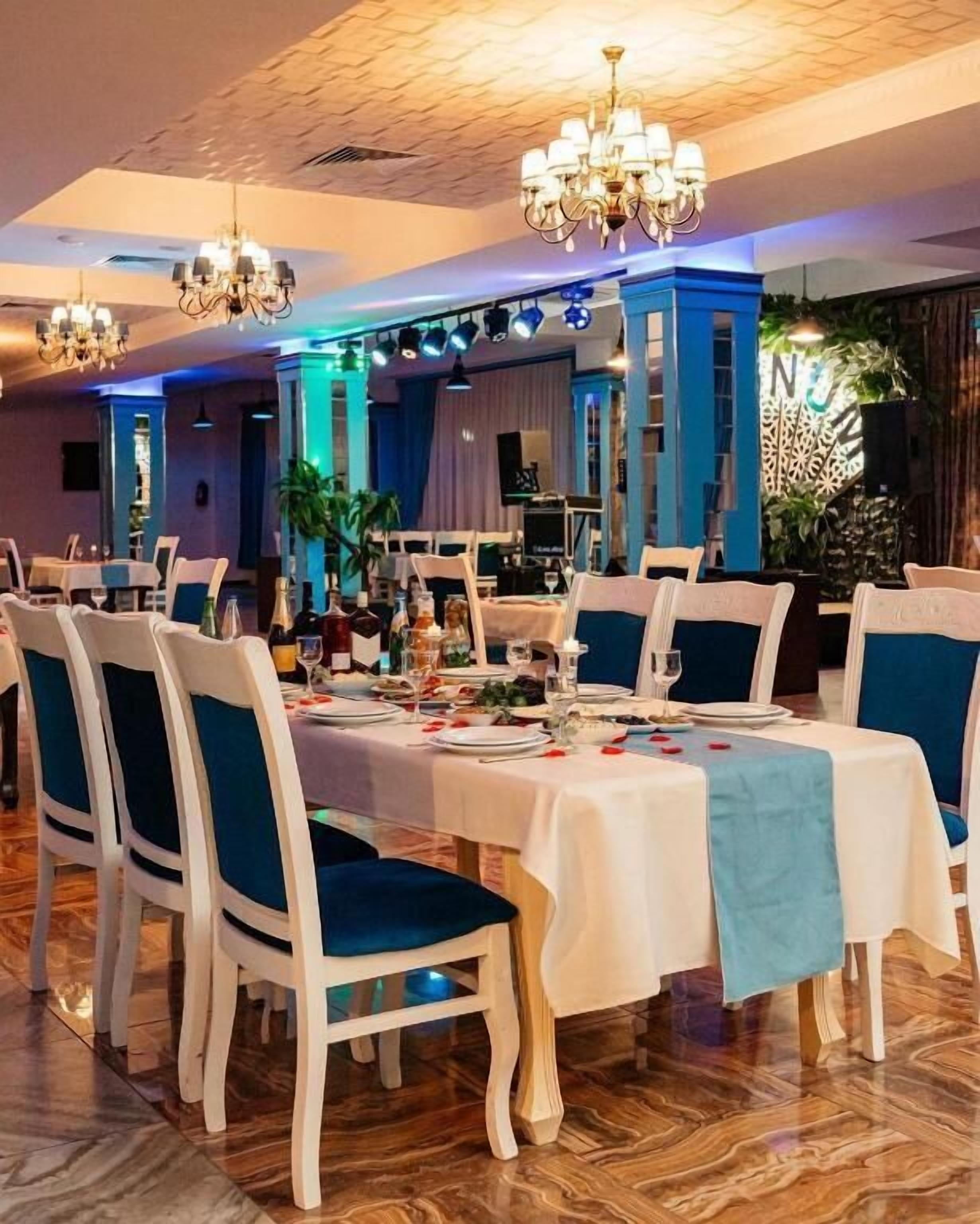 Un espace repas avec des tables dressées pour le repas, des chaises dotées de coussins bleus et des lustres.