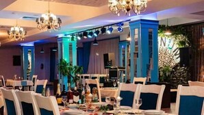 A dining area with tables set for a meal, chairs with blue cushions, and chandeliers. - Gallery & Sea Hotel (Sumqayit)