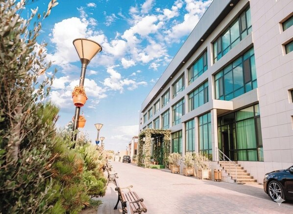 Un edificio moderno con amplios ventanales, un sendero pavimentado y mobiliario exterior.