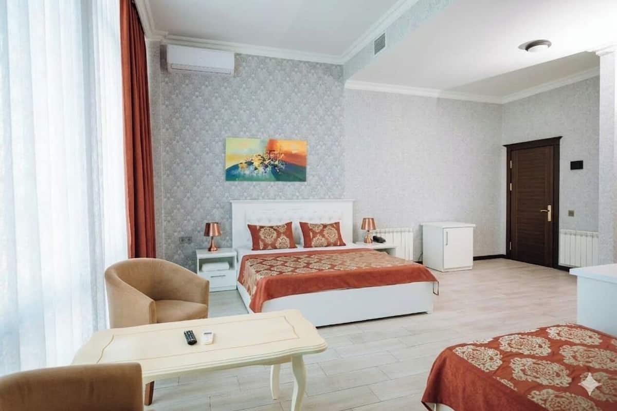 A hotel room with a bed, bedside tables, a desk, a chair, a painting, and a wardrobe.