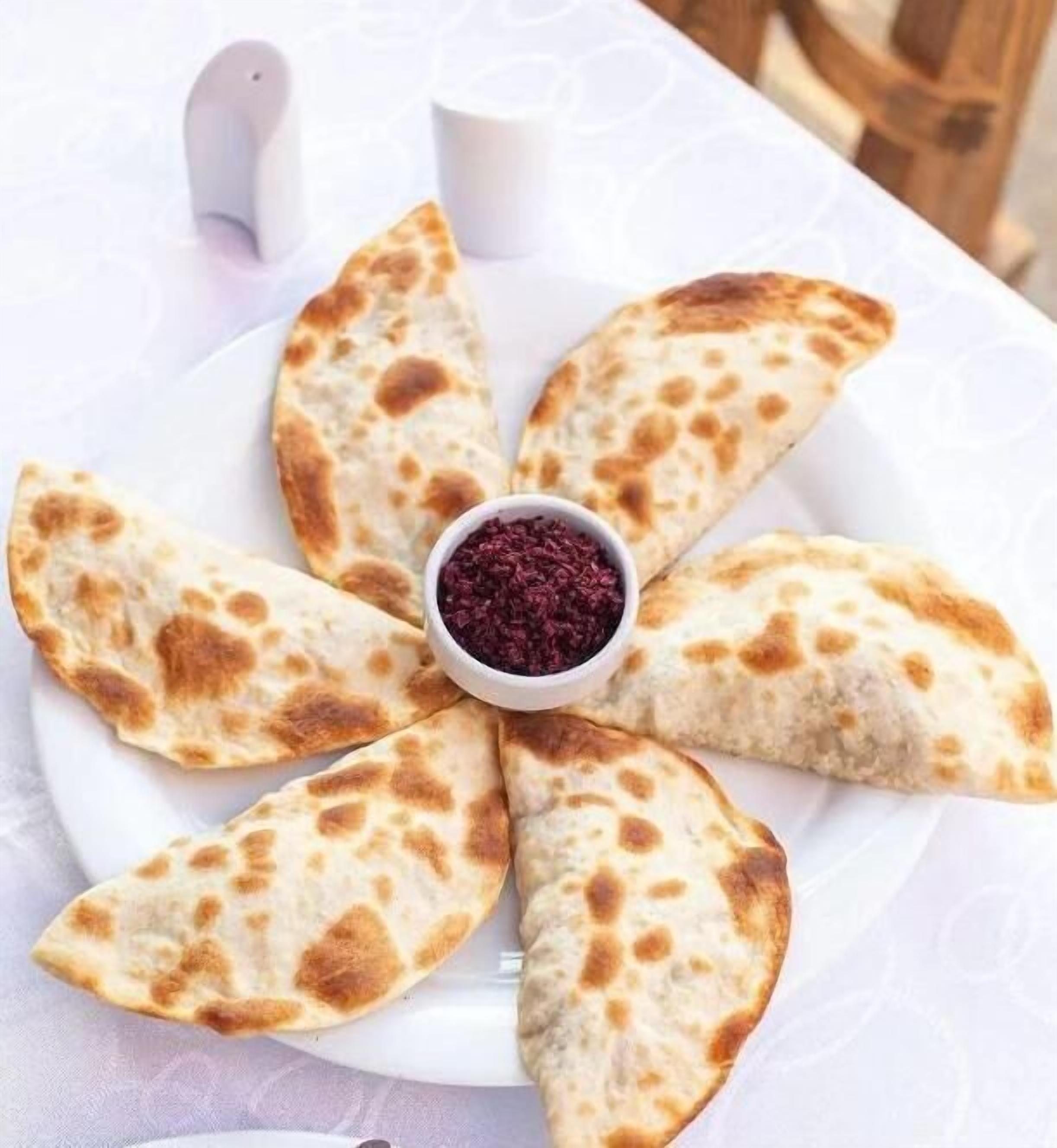 Ein Teller mit Fladenbrot, das zu einer Blumenform arrangiert ist, mit einer Schüssel roter Soße in der Mitte.