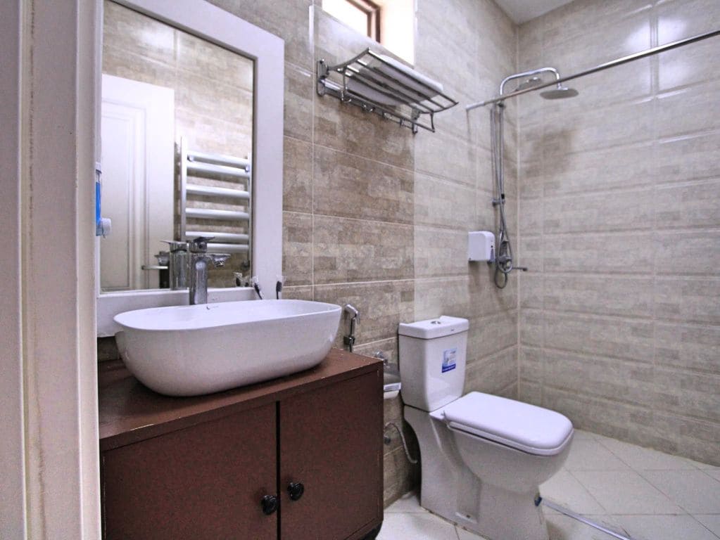 A bathroom with a white sink, a mirror, a towel rack, a toilet, and a shower area.