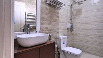A bathroom with a white sink, a mirror, a towel rack, a toilet, and a shower area.