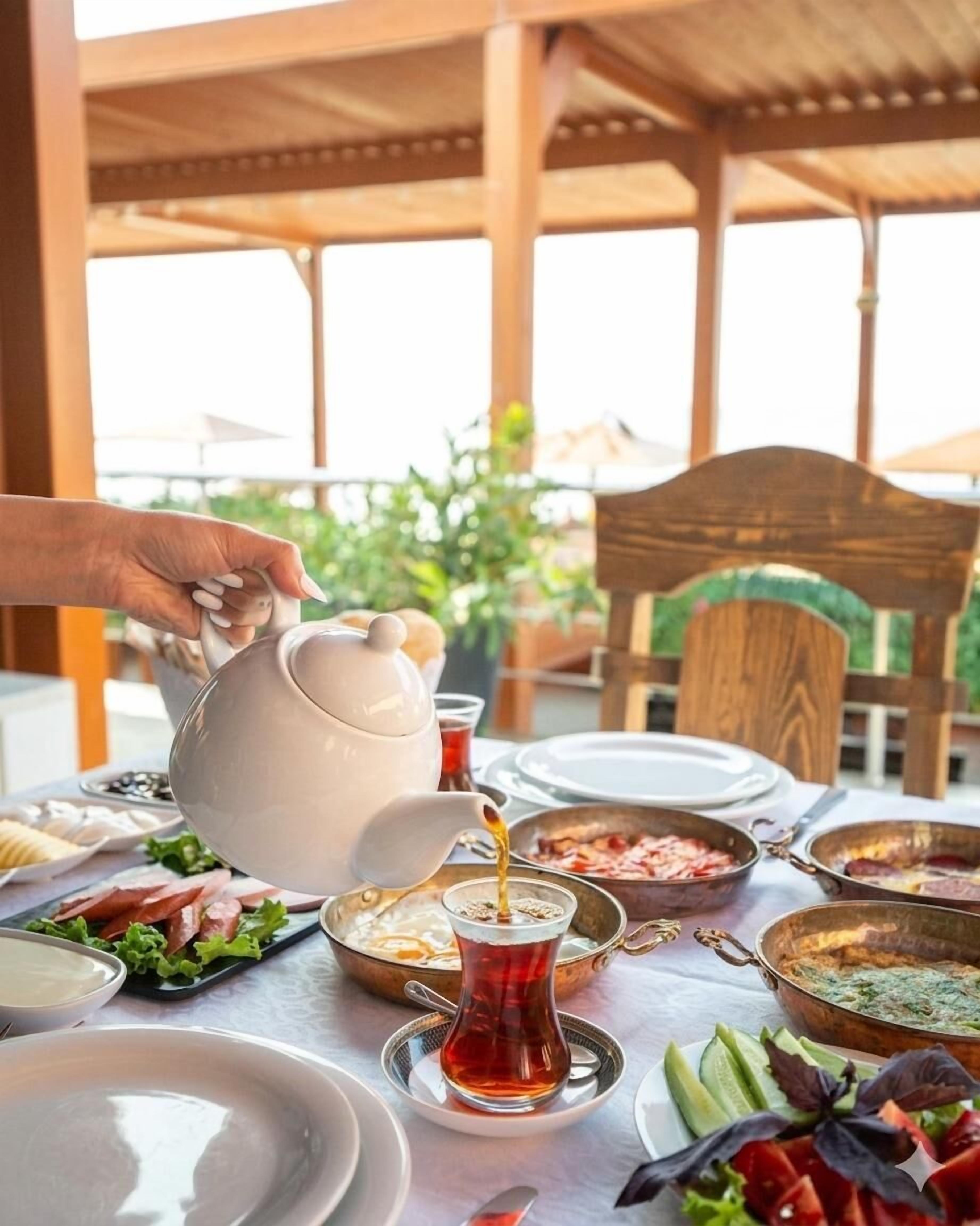 A table set for a meal with a teapot pouring tea, plates, bowls of food, and a wooden chair.