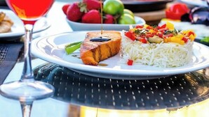 A dining table with a plate of food, a glass of red wine, and a hand pouring a sauce. - Gallery & Sea Hotel (Sumqayit)