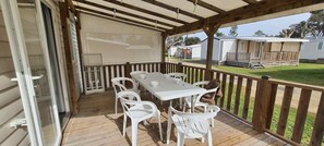 A covered outdoor patio with a table and chairs, a wooden deck, and a view of mobile homes in the background. - VVF Labenne - Océan (Labenne)