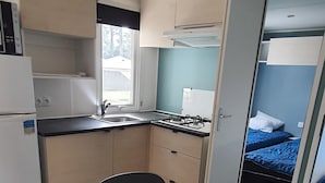 Una cocina compacta con una mesa de comedor preparada para cuatro personas, una estufa a gas y una ventana con vistas a un jardín.