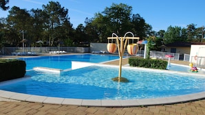 Una piscina con tobogán, sillas de descanso y una zona vallada.