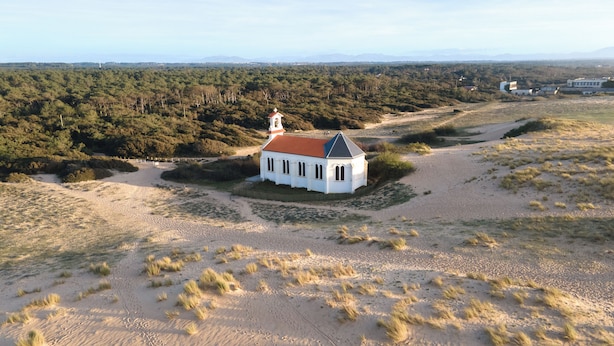 Un edificio blanco con techo rojo, rodeado de dunas de arena y vegetación escasa.
