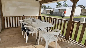 Un espacio de comedor al aire libre con techo, una mesa y sillas, vista a un jardín con césped y un edificio al fondo.