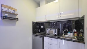 Een compacte keuken met witte kastjes, een ingebouwde vaatwasser, een magnetron en een spoelbak met kraan.