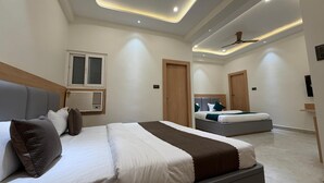 A modern hotel room with a large bed, a smaller bed, a ceiling fan, and a window with blinds. - Kailas Residency (Varanasi)