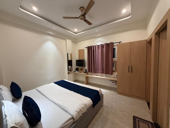 Une chambre à coucher comprenant un lit, un ventilateur de plafond, une télévision, un bureau et une armoire.