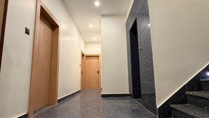 A hallway with a polished marble floor, a wooden door, and a staircase with dark tiles. - Kailas Residency (Varanasi)