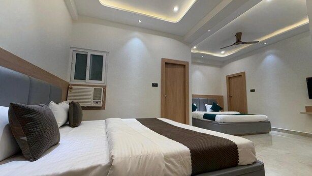 A modern hotel room with a large bed, a ceiling fan, and a window with blinds. - Kailas Residency (Varanasi)