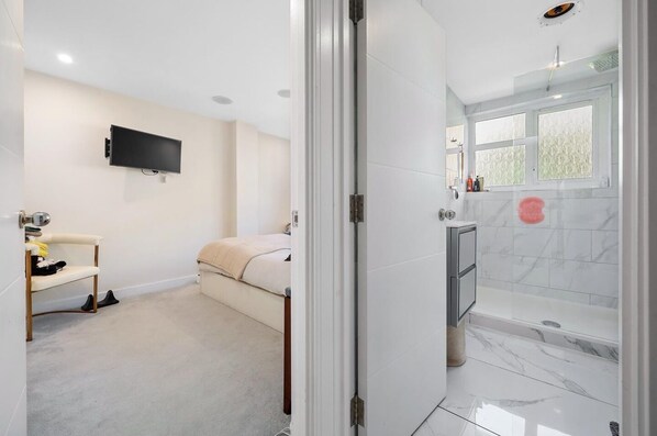 Une salle de bain moderne équipée d’une douche, de toilettes et d’un lavabo. Un téléviseur est fixé au mur et une fenêtre laisse entrer la lumière naturelle.