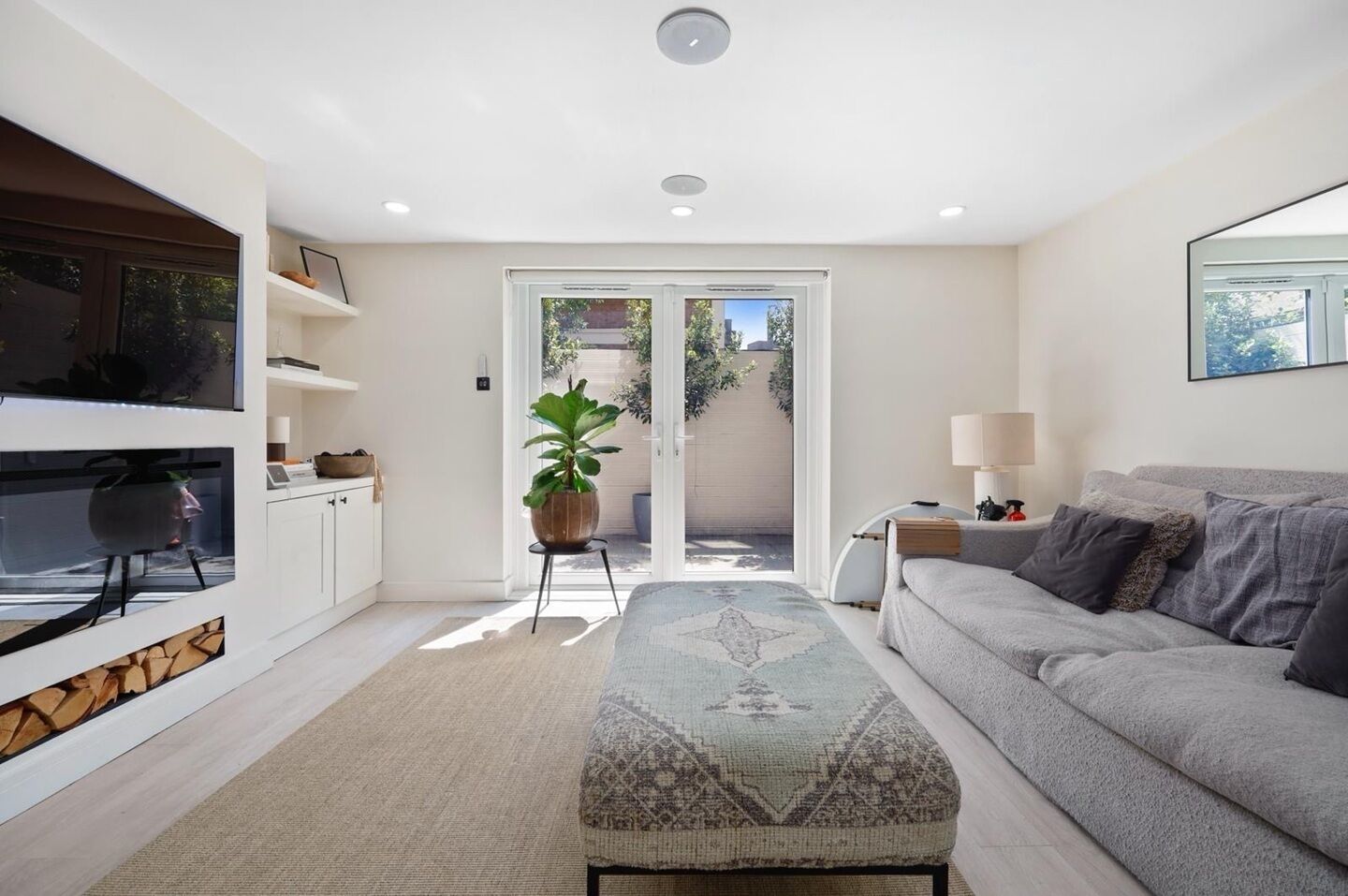 A modern living room with a sofa, a TV, a plant, and a sliding glass door leading to an outdoor area.