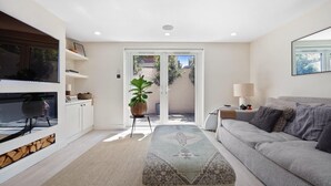 A modern living room with a sofa, a TV, a plant, and a sliding glass door leading to an outdoor area. - 
Stylish 2-Bed Split-Level Flat in Shoreditch | Short Let (Up to 1 Month) (London)