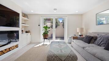 A modern living room with a sofa, a TV, a plant, and a sliding glass door leading to an outdoor area.