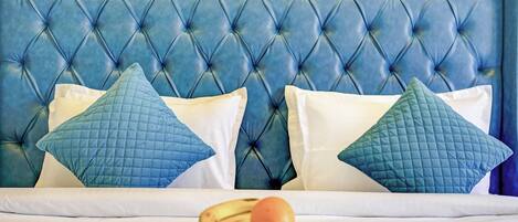 A bed with a tufted headboard, two pillows, and a wooden tray with fruits.