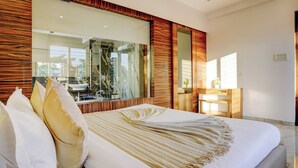 A modern bedroom with a large bed, a wooden accent wall, and a large mirror reflecting the room. - Alaya Stays Nest 4BHK villa with Pool  (Lonavala)