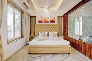 A bedroom with a large bed, a ceiling fan, a window with curtains, and a bathroom with a mirror and sink. - Alaya Stays Nest 4BHK villa with Pool  (Lonavala)