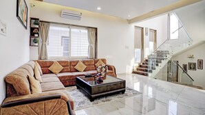 A living room with a sectional sofa, a glass coffee table, and a staircase with glass railings. - Alaya Stays Nest 4BHK villa with Pool  (Lonavala)